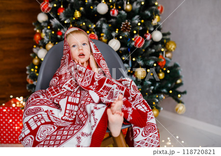 A toddler boy, aged 2, is seated in an armchair, covered with a soft blanket 118720821