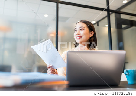 提出された書類を片手に遠くの景色を見つめながら良い発想が浮かんで笑顔になっている女性 118722185