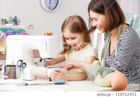 Little girl trying to make dress for her doll with her teacher 118722451