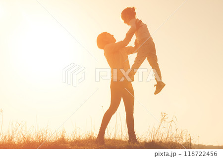 Silhouette of smilling young mother throwing up baby in the sky at sunset. Mother with child girl playing together in the field Silhouette of smilling young mother throwing up baby in the sky at sunset. Mother with child girl playing together in the field 118722456