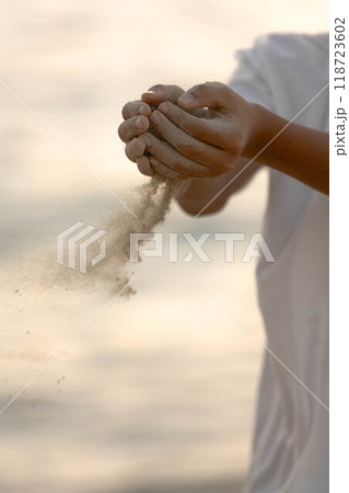 夕焼けに染まる波打ち際で砂をこぼす 118723602