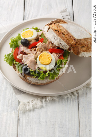 French Pan Bagnat sandwich with nicoise salad in special rye bread close-up on plate. Vertical 118725616