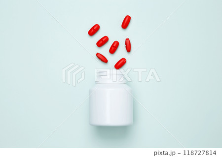 Bottles with red pills scattered on a light blue background. Concept of medicine, healthcare, and pharmaceutical industry 118727814
