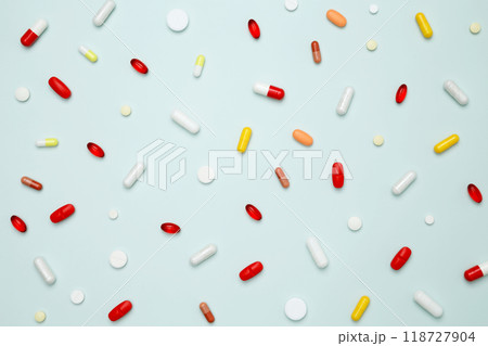 Various colorful pills and capsules scattered on a light blue background. Concept of medicine, healthcare, and pharmaceutical industry Various colorful pills and capsules scattered on a light blue background. Concept of medicine, healthcare, and pharmaceutical industry 118727904