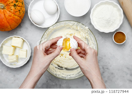 Ingredients for autumn baking. Woman breaks an egg into a bowl of dough 118727944