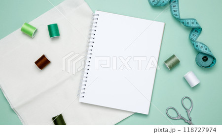 Composition with various threads and sewing accessories on green background. Mock up notebook 118727974