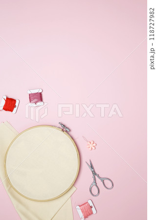 Embroidery set fot stitching. Beige cotton cloth in embroidery hoop on pink background with fabric, colorful threads, scissors and needls 118727982