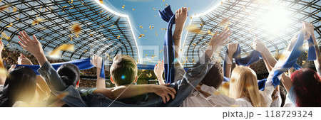 Fans dressed in blue scarves celebrate under sunlit sky, with gold confetti falling around them, while stadium's roof gleams in background. Fans dressed in blue scarves celebrate under sunlit sky, with gold confetti falling around them, while stadium's roof gleams in background. 118729324