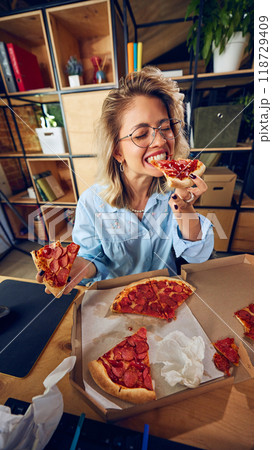 Employee eating pizza, seemingly unaware of how this habit is affecting her productivity. Messy workspace reflects poor time management. 118729409