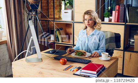 Focused on lunch, worker multitasks between bites and keyboard strokes. Eating at desk might save time, but it can hurt workflow and focus in long run. 118729420