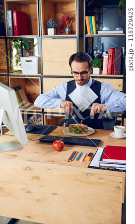 Worker enjoys sandwich while staying focused on task. Mixing food and meetings can seem efficient but might interrupt concentration. Worker enjoys sandwich while staying focused on task. Mixing food and meetings can seem efficient but might interrupt concentration. 118729425