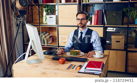 Businessman neatly sets up his desk with food. Though efficient, eating at workspace during meetings might lead to distractions. 118729431