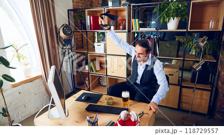 Triumphant and full of energy, businessman raises his tie in celebration, signaling small victory during challenging day of work. 118729557
