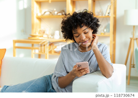 African girl holding smartphone touch screen typing scroll page at home. Woman with cell phone surfing internet using social media apps playing game. Shopping online Internet news cellphone addiction 118730674