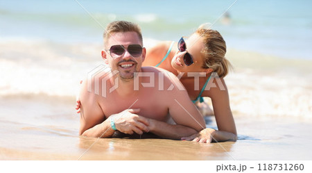 Cheerful couple resting together on beach laying on coastline and posing Cheerful couple resting together on beach laying on coastline and posing 118731260