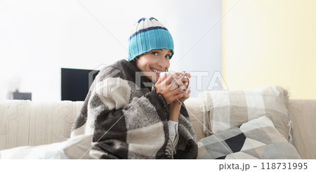 Sick woman having cup of hot tea drink covered with warm blanket Sick woman having cup of hot tea drink covered with warm blanket 118731995