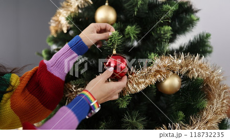 Woman in colourful sweater decorating christmas tree with red ball 118732235
