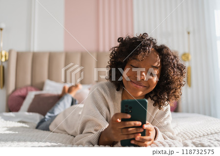 African girl holding smartphone touch screen typing scroll page at home. Woman with cell phone surfing internet using social media apps playing game. Shopping online Internet news cellphone addiction 118732575