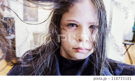 Gentle hands maneuver a hair dryer through a young girl's newly cut hair, showcasing the drying process after a meticulous trim. The warmth of the dryer breathes life into her locks, as they transform 118733181