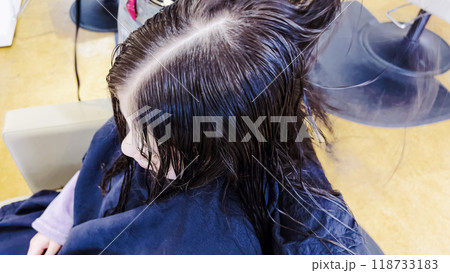 Gentle hands maneuver a hair dryer through a young girl's newly cut hair, showcasing the drying process after a meticulous trim. The warmth of the dryer breathes life into her locks, as they transform 118733183