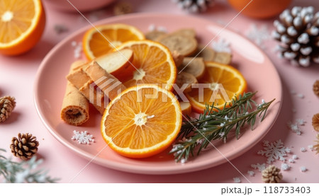 A festive plate of orange slices, cinnamon sticks, and pinecones is arranged decoratively, symbolizing a holiday or winter theme. The image is warm and seasonal. 118733403