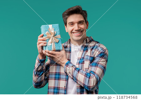 Handsome Man Holding Gift Box On Blue Studio Background And Smiles To Camera 118734568