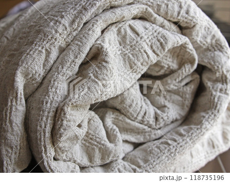 A rolled-up blanket, a bedspread, a plaid made of linen. Creating a cozy and warm home in the style of Hygge. Textile industry, knitting. Background, texture with fabric, drapery 118735196