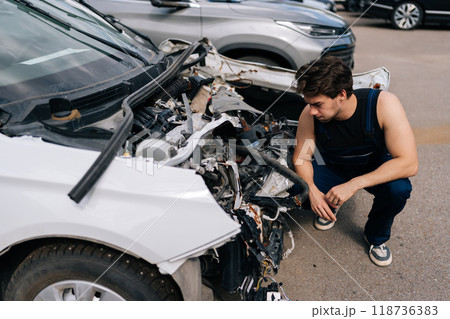 High-angle view of pensive mechanic examining front of car without bumper, assessing plan for future work in automobile repair and renew service station. Concept of car service, repair and maintenance High-angle view of pensive mechanic examining front of car without bumper, assessing plan for future work in automobile repair and renew service station. Concept of car service, repair and maintenance 118736383