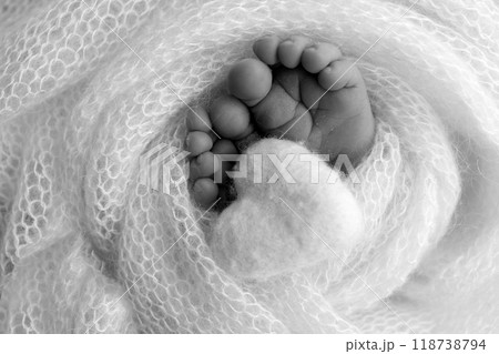 The tiny foot of a newborn baby. Soft feet of a new born in a wool blanket. Close up of toes, heels and feet of a newborn. Knitted heart in the legs of a baby Studio macro photography. Black and white The tiny foot of a newborn baby. Soft feet of a new born in a wool blanket. Close up of toes, heels and feet of a newborn. Knitted heart in the legs of a baby Studio macro photography. Black and white 118738794