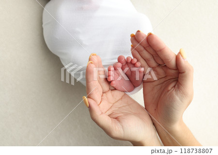 The palms of the parents. A father and mother hold the feet of a newborn child in a white blanket on a white background.. The feet of a newborn in the hands of parents. Photo of foot, heels and toes The palms of the parents. A father and mother hold the feet of a newborn child in a white blanket on a white background.. The feet of a newborn in the hands of parents. Photo of foot, heels and toes 118738807