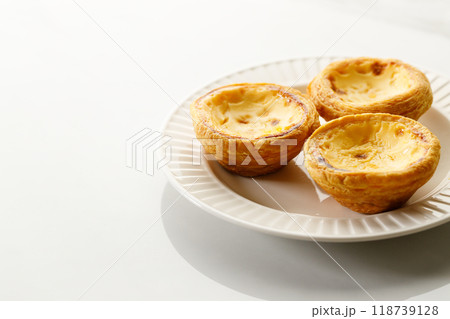 Stack of Portuguese sweet dessert egg tart or Pastel de Nata on white ceramic plate on white table. Copy space. Selective focus. 118739128