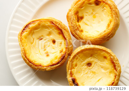Stack of Portuguese sweet dessert egg tart or Pastel de Nata on white ceramic plate on white table. Copy space. Selective focus. 118739129