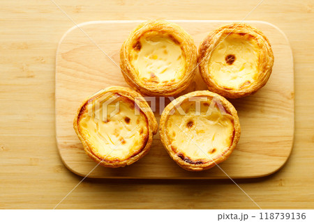 Stack of Portuguese sweet dessert egg tart or Pastel de Nata on wooden board on wooden table. Selective focus. Top view. Stack of Portuguese sweet dessert egg tart or Pastel de Nata on wooden board on wooden table. Selective focus. Top view. 118739136