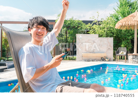 プールサイドでリクライニングチェアに座りゲームをする若いアジア人男性 118740555