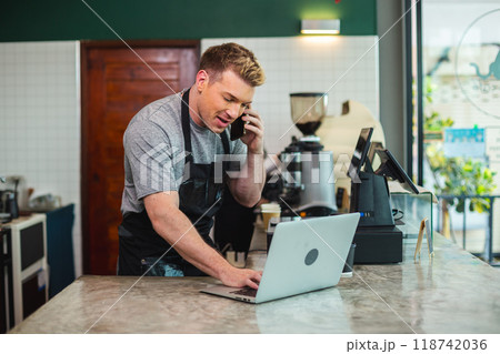 Young men barista wear apron talking telephone and using laptop computer 118742036