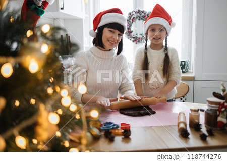 Mother and daughter baking cookies wearing Santa hats Mother and daughter baking cookies wearing Santa hats 118744276