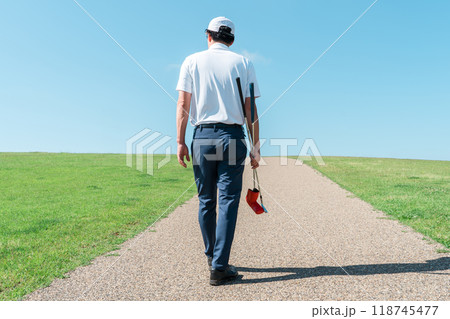 パターとゴルフクラブを持ってゴルフ場を歩く男性の後ろ姿 パターとゴルフクラブを持ってゴルフ場を歩く男性の後ろ姿 118745477