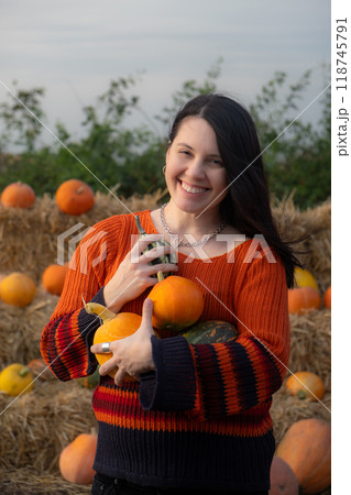 Woman holding a pumpkin sitting on hay bales Woman holding a pumpkin sitting on hay bales 118745791