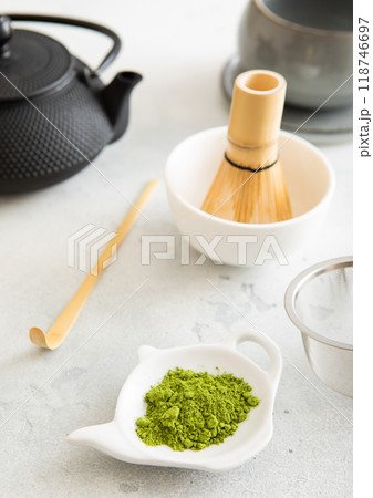 Matcha green tea powder with bamboo spoon and whisk in ceramic bowl with iron kettle on white background. Matcha green tea powder with bamboo spoon and whisk in ceramic bowl with iron kettle on white background. 118746697
