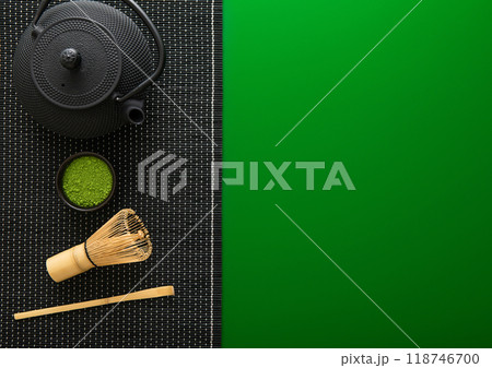 Organic matcha green tea powder with bamboo whisk and spoon and japanese traditional iron cast kettle on green background.Top view. 118746700