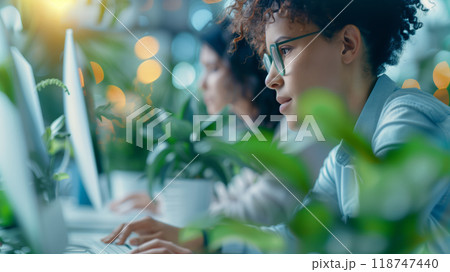 Focused professionals working on computers in a modern office with indoor plants, highlighting concentration and productivity. 118747440
