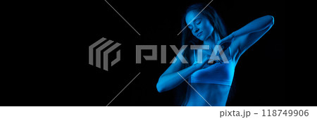 Portrait of beautiful young girl with long hair, slim, skinny body shape, posing in underwear against black background in neon light 118749906