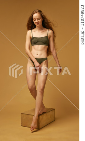 Full-length portrait of tender young woman with slim, beautiful body shape, posing in underwear against sandy color studio background Full-length portrait of tender young woman with slim, beautiful body shape, posing in underwear against sandy color studio background 118749923