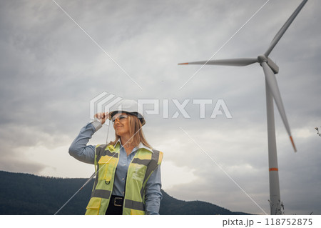 A confident and skilled female engineer working at a wind farm, she is a dedicated professional in the renewable energy sector, committed to promoting sustainability through teamwork and innovation 118752875