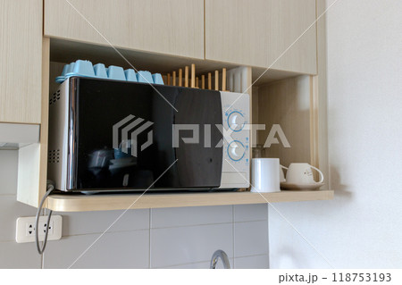 black-and-white microwave placed on a wooden kitchen shelf.  118753193