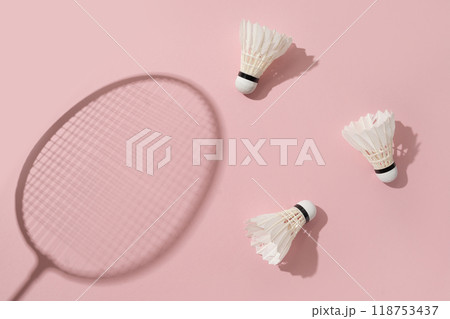 White badminton shuttlecocks and badminton rackets as shadow on pink background. View from above. Creative concept racket sport. Leisure games. White badminton shuttlecocks and badminton rackets as shadow on pink background. View from above. Creative concept racket sport. Leisure games. 118753437