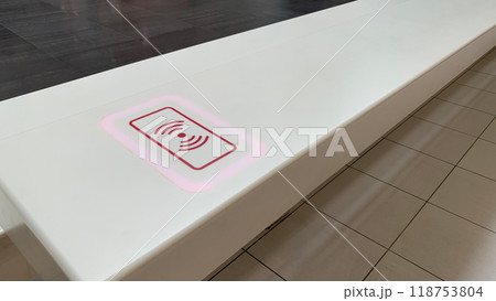 Tabletop with sticker indicating place for wireless charging of phone, modern electricity technologies for charging device without wire, put down phone on surface and charge battery Tabletop with sticker indicating place for wireless charging of phone, modern electricity technologies for charging device without wire, put down phone on surface and charge battery 118753804