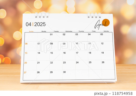 April 2025 desk calendar on wooden table with gold light bokeh background. 118754958