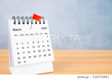 March 2025 calendar and red push pin on table. 118754961