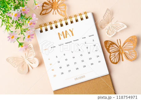 May 2025 desk calendar and paper butterfly with flower. 118754971